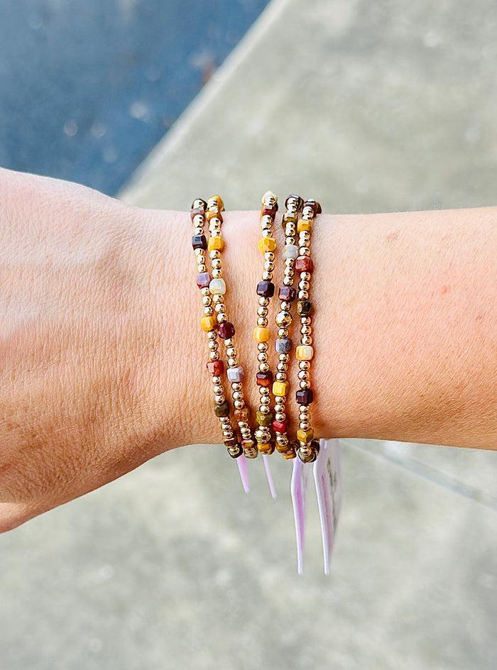 Gold filled beaded bracelets featuring colorful gemstone cube beads stacked on a wrist