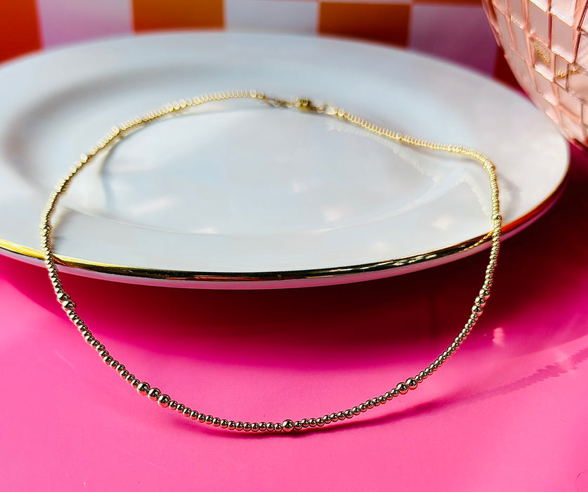 Remi gold filled beaded necklace displayed on a white plate